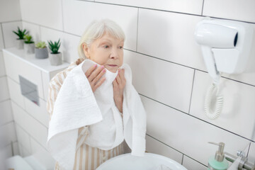 Gray-haired woman drying her face with the towel