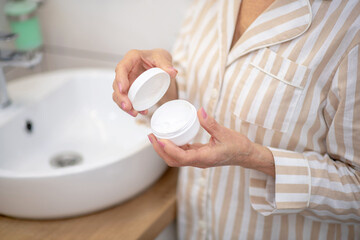 Close up picture of a woman with a jar of cream in hands