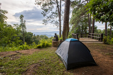 the man sitting in fron of his tent looking out to the mountain with sky and tree surrounded
