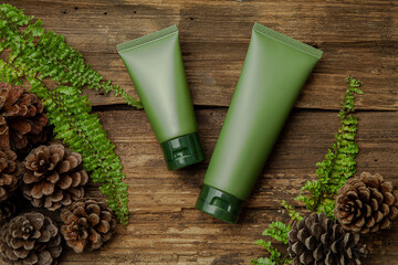 Green cosmetic tubes  with green leaves on wood background. Blank label for branding mock-up....