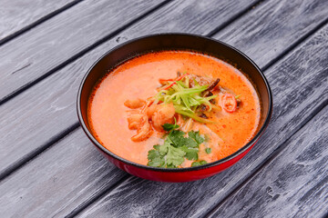Soup with seafood and shrimps served in a black bowl over rustic wooden background.