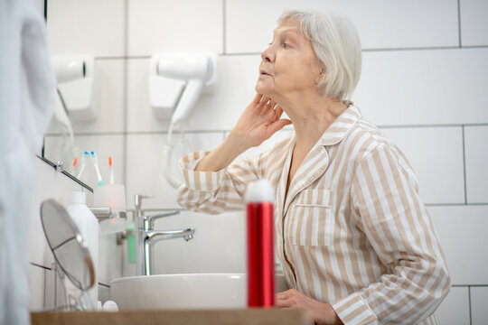 Gray-haired Woman In Pajama Doing Hair In The Bathroom