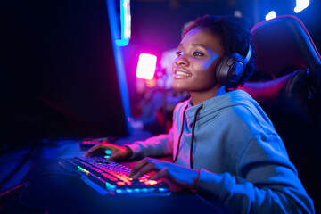 Professional Streamer African young woman cyber gamer studio room with personal computer armchair, keyboard in neon color blur background - obrazy, fototapety, plakaty