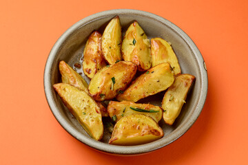 Baked potato with rosemary served in a ceramic bowl over orange background. Delicious idea for dinner.