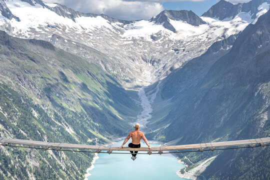 Half naked male sit on swing bridge viewing glacier in Zillertal Alps in summer