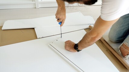 Furniture assembly process. A man is assembling the drawer for the wardrobe via screwdriver.
