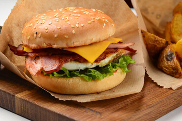 Tasty cheeseburger with fried potatoes rustic style, with sauce, served on a wooden board over white background.