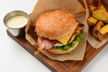 Tasty cheeseburger with fried potatoes rustic style, with sauce, served on a wooden board over white background.