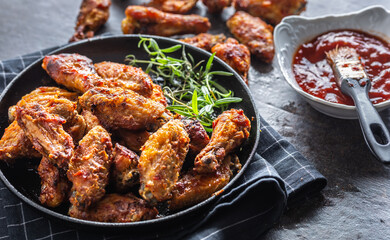 Chicken wings barbeque in a cast iron baking dish with BBQ sauce and rosemary