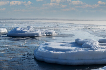 Snow-white ice floes and frozen rocks sticking out of the sea on a frosty sunny day.