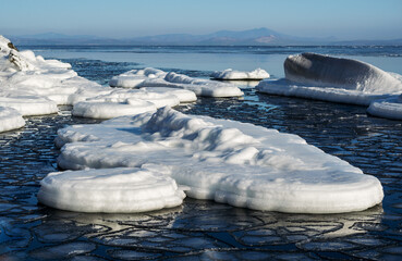 Snow-white ice floes and frozen rocks sticking out of the sea on a frosty sunny day.