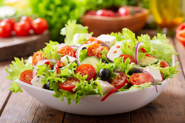 Bowl of fresh salad with vegetables, feta cheese and olives on a wooden table