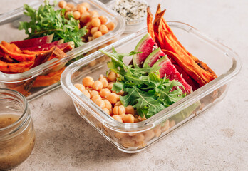 Vegan healthy meal prep containers. Chickpeas, sweet potatoes, arugula, radish, avocado and sauce for lunch on concrete background. Vegan, healthy, detox food concept. Selective focus