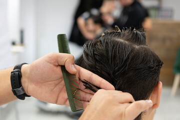 Male client getting haircut by hairdresser with comb and scissors