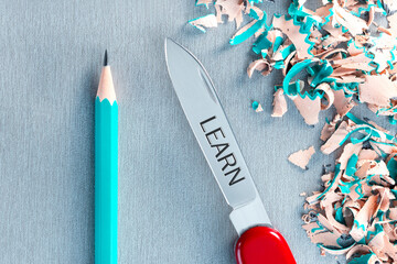 Learn concept. Ideal planed pencil and penknife with LEARN text on gray surface. Top view.