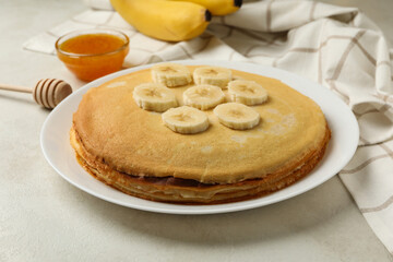 Concept of breakfast with plate of thin pancakes with banana, and jam on white textured background