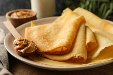 Concept of delicious breakfast with plate of crepes with peanut butter on wooden board