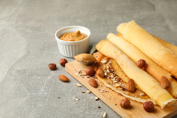 Concept of delicious breakfast with crepes with peanut butter and nuts on gray table