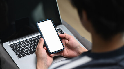 Rear view of young man working with laptop computer and using mobile phone in office.