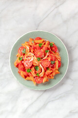 Penne pasta with chicken, tomatoes and parsley, top shot on a white marble background with a place for text