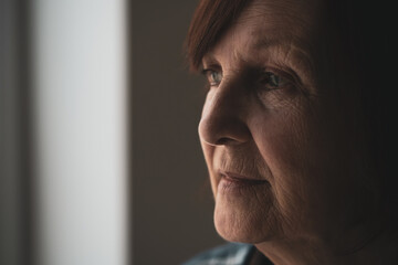 Close-up portrait of senior woman with dementia who is looking through window.