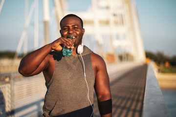 Portrait of young cheerful african-american man in sports clothing who is drinking water after exercise. He is exercising to reduce his body weight. 