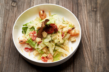 Caesar salad with shrimp on white bowl, on table