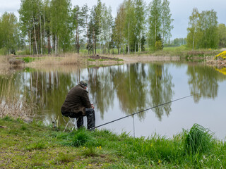 Fototapeta na wymiar landscape with a fisherman on the shore of the lake, fishing accessories in the green hall are in the foreground