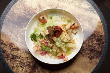 Caesar salad with shrimp on white bowl, on table