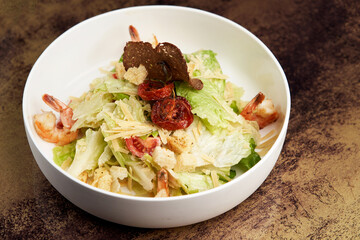 Caesar salad with shrimp on white bowl, on table
