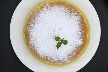 Cheesecake decorated with icing sugar and mint in a white plate