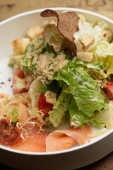Caesar salad with salmon fish on white bowl