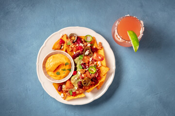 Nachos with chili con carne and a Paloma cocktail, top shot on a blue background