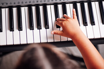 top view of a head and a girl's hand playing a tune on an electronic synthesizer in the living room.