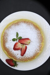 Cheesecake decorated with icing sugar, mint and strawberry in a white plate