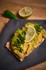 healthy vegan breakfast. avocado toast with lime and coriander on top of a dark napkin on a wooden background. diet foot