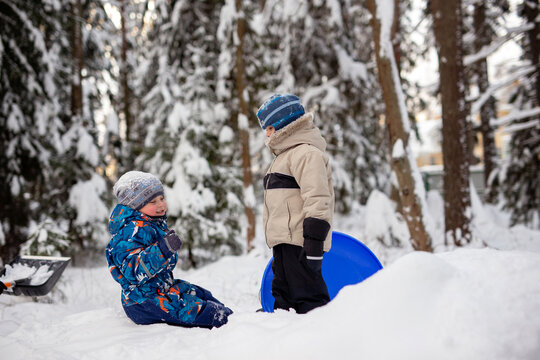 cute caucasian boys playing on fresh air on winter day, one is holding snow sled. Image with selective focus