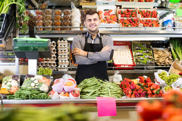 Smiling male seller showing assortment of fruits and vegetables in the grocery shop