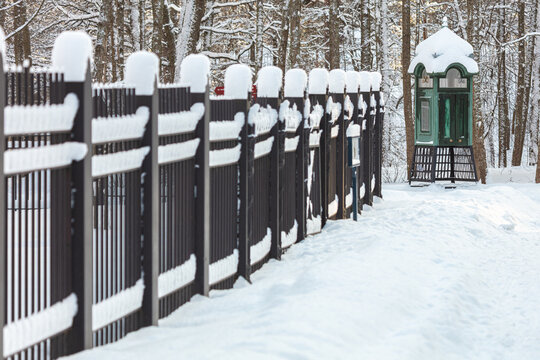 An iron fence, covered with snow in winter, against the background of an old telephone booth. Finnish nature and architecture. Seurasaari, Helsink