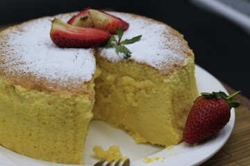 Cheesecake decorated with icing sugar, mint and strawberry in a white plate