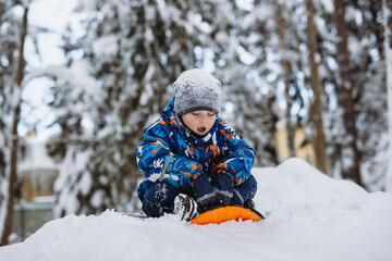 Fototapeta na wymiar A cute caucasian boy preparing to go down the snow slide. Winter fun and healthy things to do