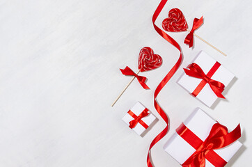 Valentines day background - white gift boxes with red silk bow, ribbon, lollipops hearts on white wood table, copy space.