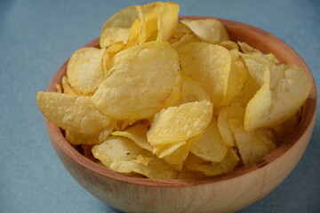 Crispy potato chips in bowl on blue background