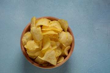 Crispy potato chips in bowl on blue background