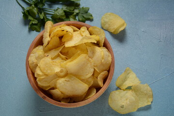Crispy potato chips in bowl on blue background
