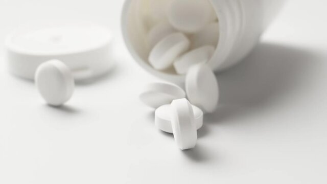 White tablets fall out of the bottle onto the table, slow motion. Antiviral drugs, virus protection, Covid-19 treatment.
