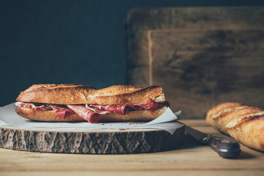 Jam&oacute;n ib&eacute;rico in a bread baguette ion a wooden board and in a low key atmosphere.