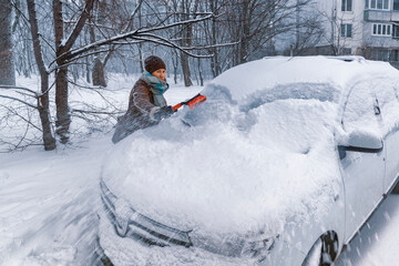 Woman driver cleans windshield of her car from snow.