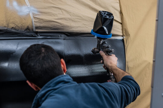 A professional mechanic working in a paint chamber during the coating process of a damaged vehicle. Airbrush technology, high-pressure painting, restyling, automotive wrapping service.