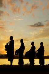 Fototapeta na wymiar silhouette of monks dressing orange robe during reception of alms, on the shore of the mekong river 